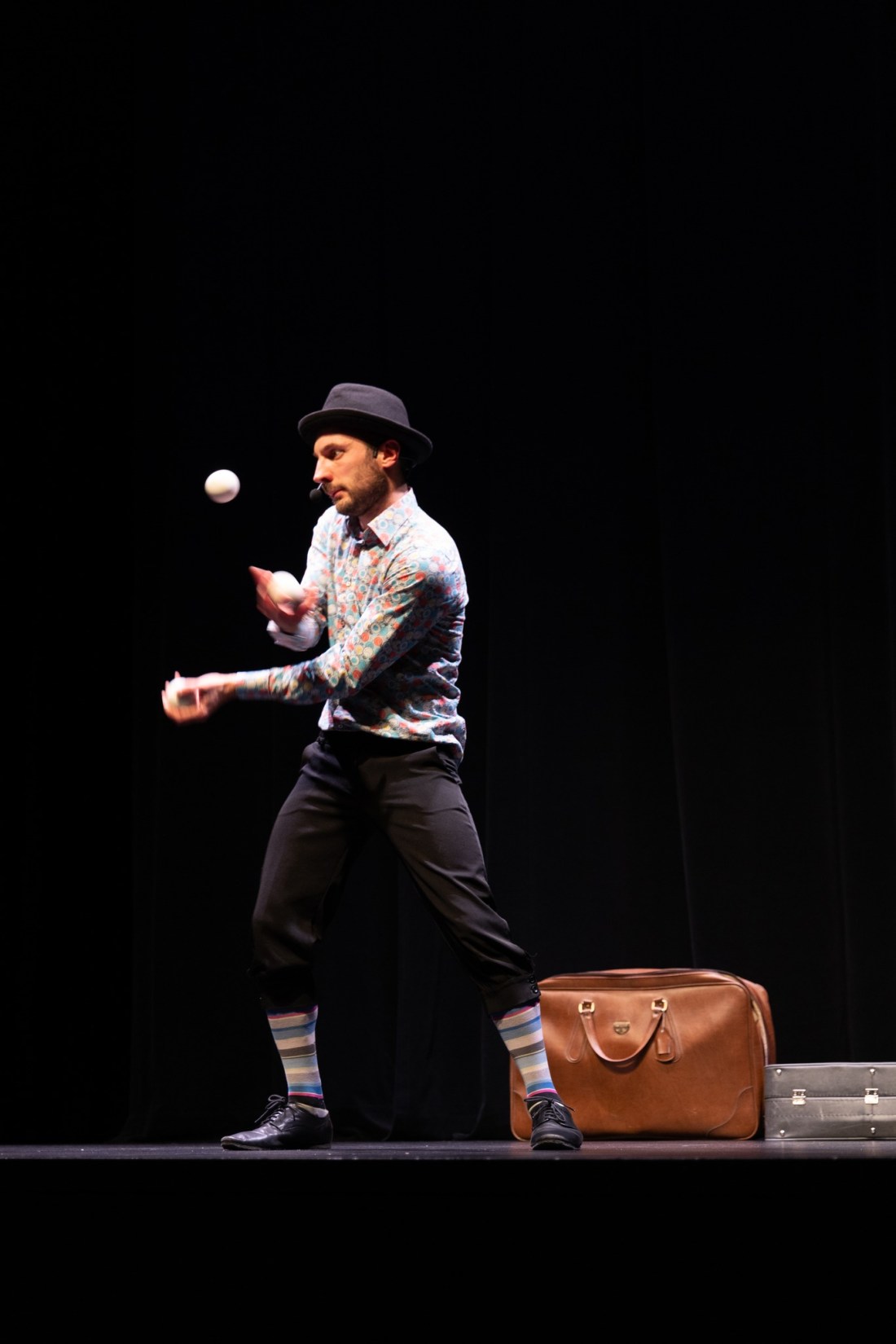 Jongleur de balles sur la scène d’un théâtre, en intérieur, avec un arrière-plan entièrement noir.