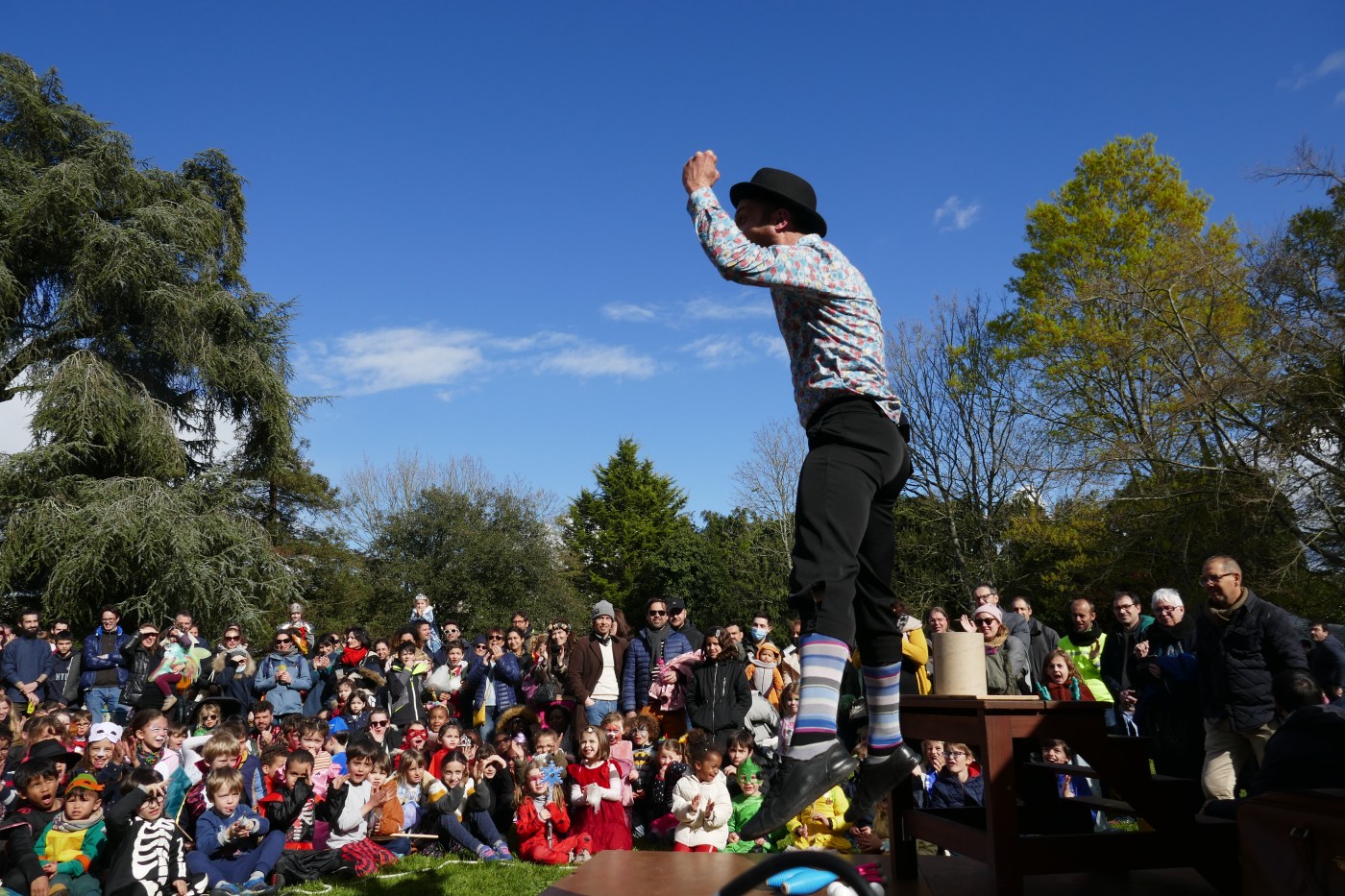 Artiste de cirque qui saute devant un large public, composé principalement d’enfants, lors d’un spectacle en extérieur.